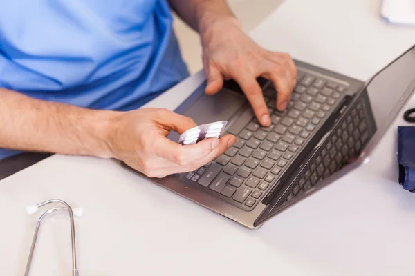 Doctor using laptop and holding pills — Stock Photo, Image