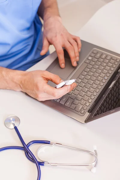 Médico usando laptop e segurando pílulas — Fotografia de Stock