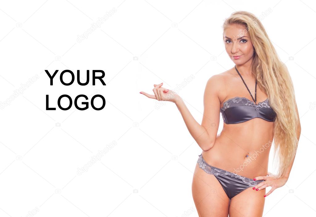 Beautiful sexy blonde model with lovely wavy long hair and a curvaceous body posing in purple lingerie. She is pointing copy space. Your logo.