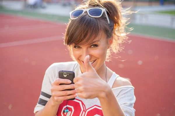 Flicka håller telefonen och visar tummen upp — Stockfoto