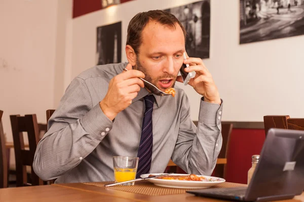 Empresario comiendo y hablando por teléfono — Foto de Stock