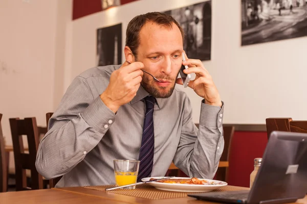 Businessman eating and talking on phone — Stock Photo, Image