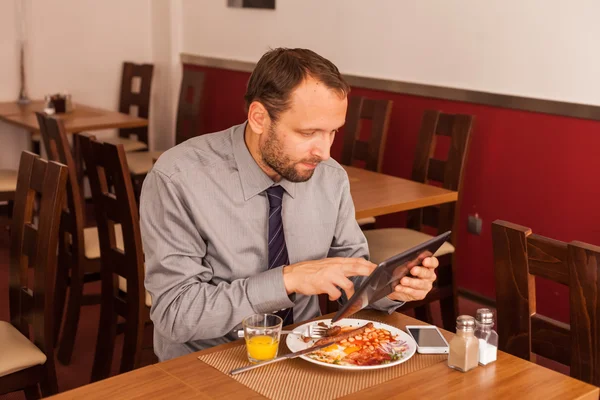 Бизнесмен использует планшет во время еды — стоковое фото