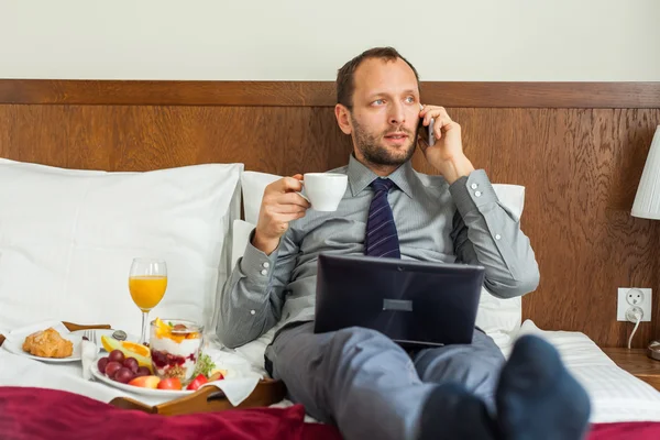 Empresario usando teléfono y portátil durante el desayuno —  Fotos de Stock