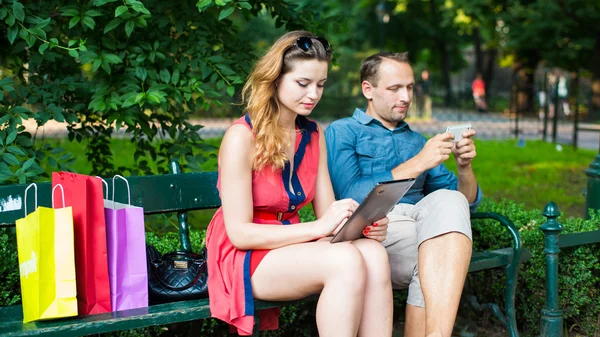 Couple assis sur le banc et utilisant des gadgets numériques — Photo