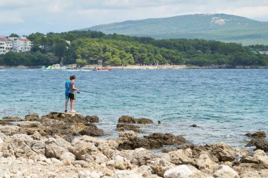 Krk, Hırvatistan 05 Ağustos 2021: Hırvatistan 'ın Krk kenti yakınlarındaki kayalık sahilde iki çocuk balık tutuyor                               