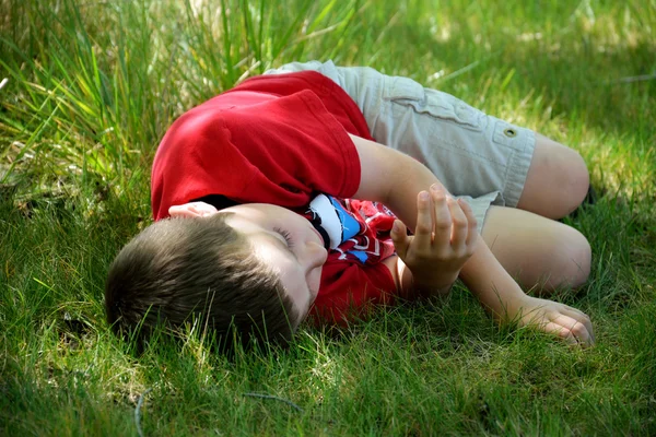 Boy taking nap on grass under shaded tree