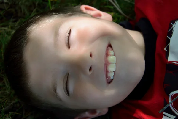 Niño tendido en la hierba sonriendo fingiendo estar dormido —  Fotos de Stock