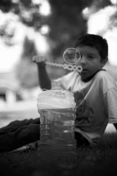 Boy sitting in grass blowing bubbles — Stock Photo, Image