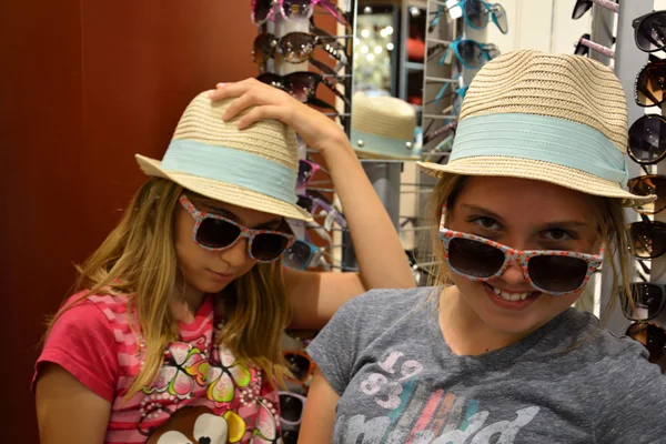 Girls playing dress up in store with hats and sunglasses — Stock Photo, Image