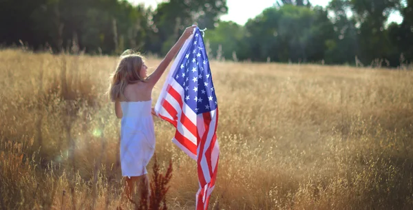 Pige går i gyldne felt holder amerikansk flag - Stock-foto