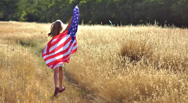 Pige kører i gyldent felt holder amerikansk flag - Stock-foto