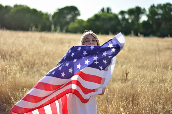 Girl holding American flag walking in golden field — Stock Photo, Image