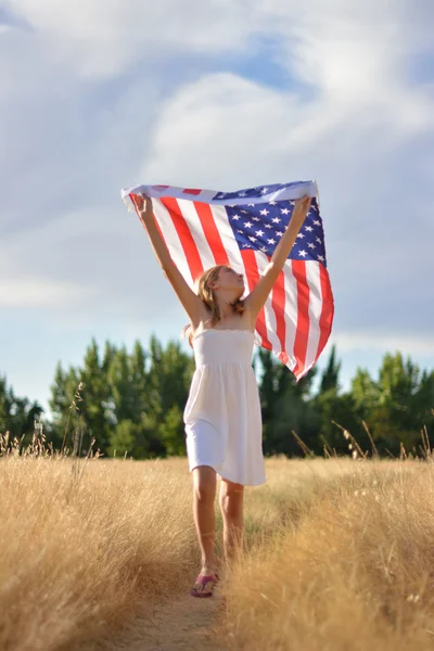 Girl running in golden field holding American flag — Stock Photo, Image