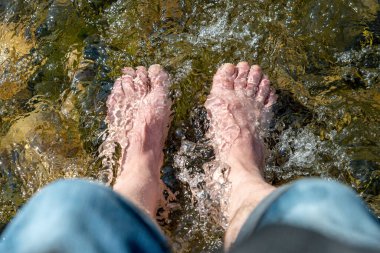 Flowing water between stones laps a mans feet in the sunshine in the summer