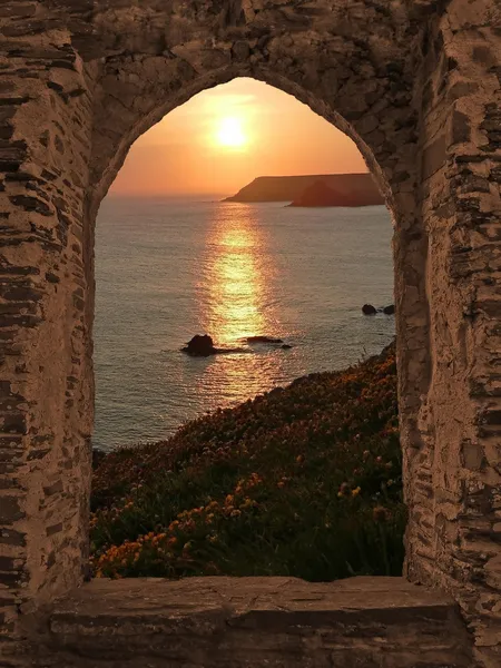 Bekijken door gebogen kasteel raam naar zonsondergang kustlandschap, cornwall — Stockfoto