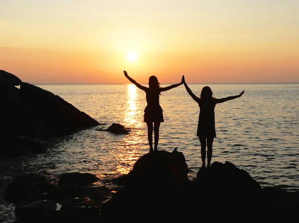 Two silhouette girls standing at the rocky seaside on sunset — Stock Photo, Image