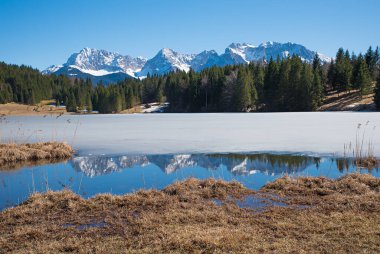 Donmuş Geroldsee Gölü, göl kıyısında berrak suyla, Karwendel Dağları 'nı yansıtıyor,