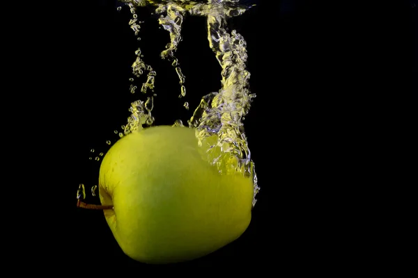 Green apple in yellow splash isolated on black background — Stock Photo, Image