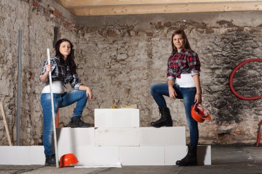 iki genç uzun saçlı kadın bloklarla yeni bir duvar inşa edilmiş.