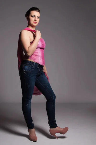 Jonge vrouw in roze korset, jeans, hoge hakken met roze sjaal — Stockfoto