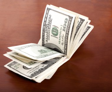 100 ABD Doları Bonosu yığın kahverengi zemin üzerinde katlanmış.