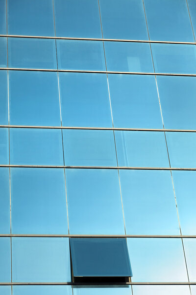 Cloudy sky reflecting off an office building curtain wall made of identical square windows, with one window open.