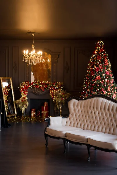 Interior of luxury dark living room with fireplace, comfortable sofa and chandelier decorated with Christmas tree and gifts — Stock Photo, Image