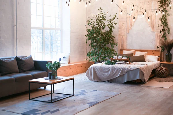 大きなパノラマウィンドウと緑の植物とロフトスタイルで無料のレイアウトを持つ豪華なスタジオアパートメントで居心地の良いベッドルームエリア. — ストック写真