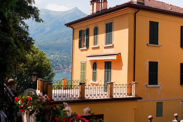 İtalya 'nın eski Bellagio kasabasında Como Gölü' nde sarı bir ev ve arkasında dağlar var..
