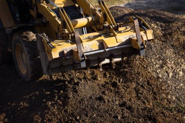 Kazıcı çukuru ön kovayla dolduruyor ve toprağı inşaat alanının etrafına taşıyor. Yakın plan. Ağır inşaat ekipmanları
