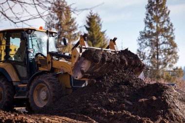 Kazıcı çukuru ön kovayla dolduruyor ve toprağı inşaat alanının etrafına taşıyor. Yakın plan. Ağır inşaat ekipmanları