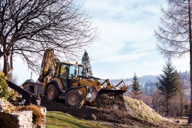 Kazı makinesi ön kovayla çukuru dolduruyor. İnşaat alanında toprağı hareket ettiriyor. Ağır inşaat ekipmanları