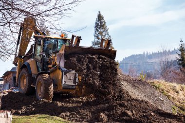 Kazı makinesi ön kovayla çukuru dolduruyor. İnşaat alanında toprağı hareket ettiriyor. Ağır inşaat ekipmanları