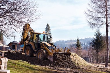 Kazı makinesi ön kovayla çukuru dolduruyor. İnşaat alanında toprağı hareket ettiriyor. Ağır inşaat ekipmanları