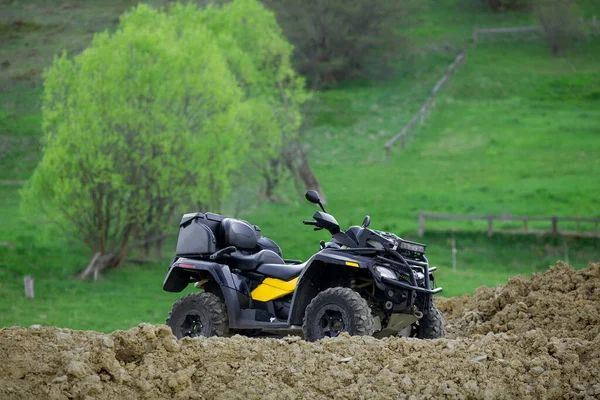 A four-wheeled ATV quad bike standing idle on the green grass, with trees and a mountain on the background. — Stock Photo, Image