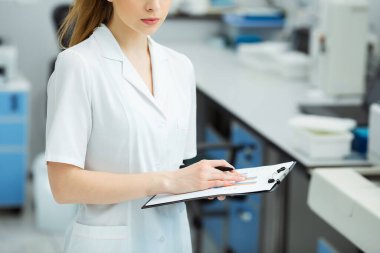 Modern laboratuarda tıbbi araştırma yapan çekici kadın bir laboratuvar çalışanı. Analiz sonuçlarıyla birlikte belge dizini tutan bilim adamı