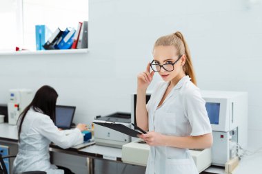 Modern laboratuarda tıbbi araştırma yapan çekici kadın bir laboratuvar çalışanı. Analiz sonuçlarıyla birlikte belge dizini tutan bilim adamı