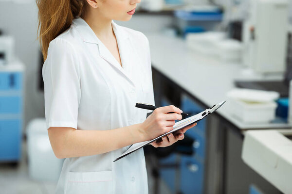 Attractive female lab worker making medical research in modern laboratory. Scientist holding documents folder with analysis results