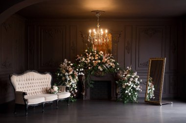 Black classical room interior with a vintage sofa, chandelier, mirror and fireplace decorated with flowers