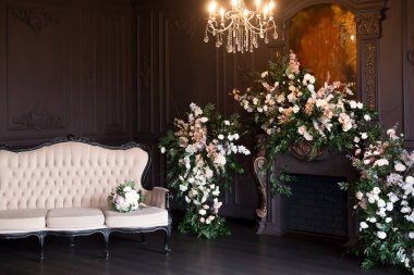 Black classical room interior with a vintage sofa, chandelier, mirror and fireplace decorated with flowers