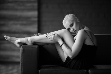 Sadness, depression and loneliness concept. Portrait of sad blonde girl with a short stylish haircut sitting alone on a dark background