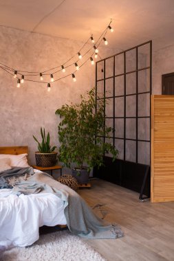 Cozy bedroom area at luxury studio apartment with a free layout in a loft style with big panoramic window and green plant.Soft focus image contain film grain