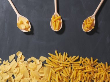 Farklı şekillerde ham makarna ve koyu arkaplanda lezzetli makarna.
