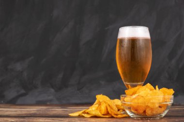 Koyu ahşap arka planda bir kase cipsin yanında taze çekilmiş hafif bira bardağı.
