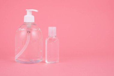 El dezenfektanı sıvısı, anti bakteriyel alkol sıvısı şeffaf plastik bir şişede pembe arka planda.