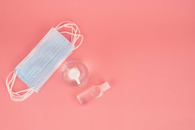 Tıbbi ağız maskesi ve el dezenfektanı, pembe arka planda Coronavirus 'a (Covid-19) karşı korunmak için önemli bir ilave.