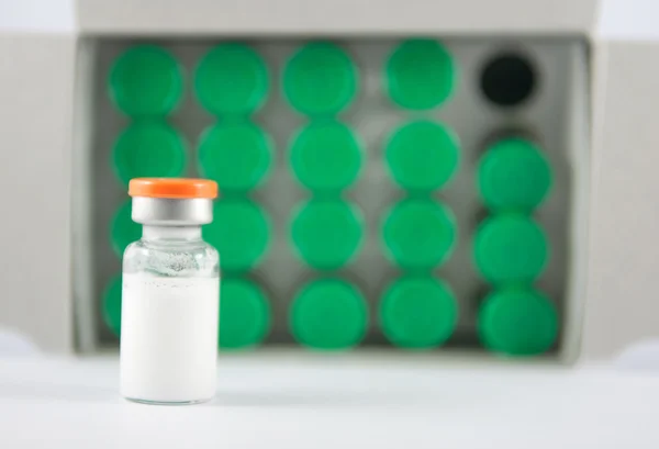 Bílý odpruženou v injekční lahvičky na pozadí zelených lahvičky — Stock fotografie