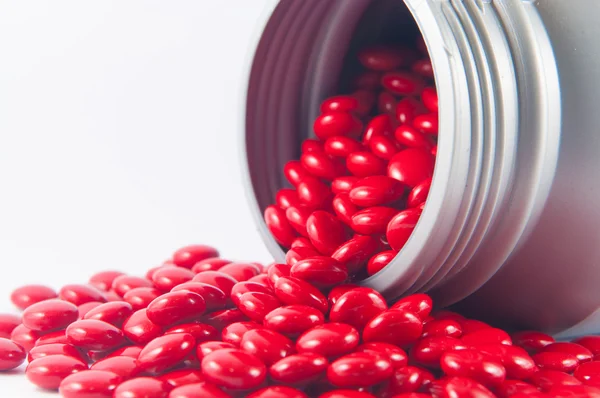 Coated red tablet and gray plastic bottle on white show medicine — Stock Photo, Image