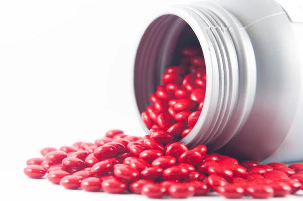 Comprimé rouge enrobé et bouteille en plastique gris sur le médicament show blanc — Photo